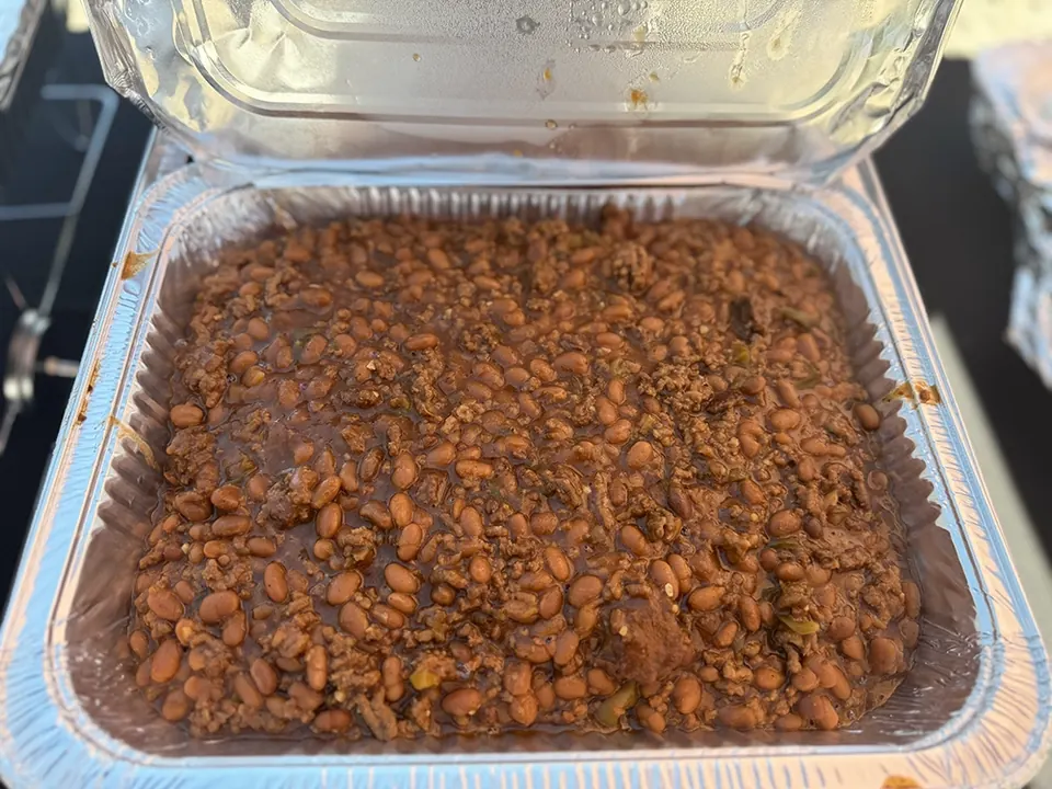 Baked beans in a foil pan beneath a chafing dish lid