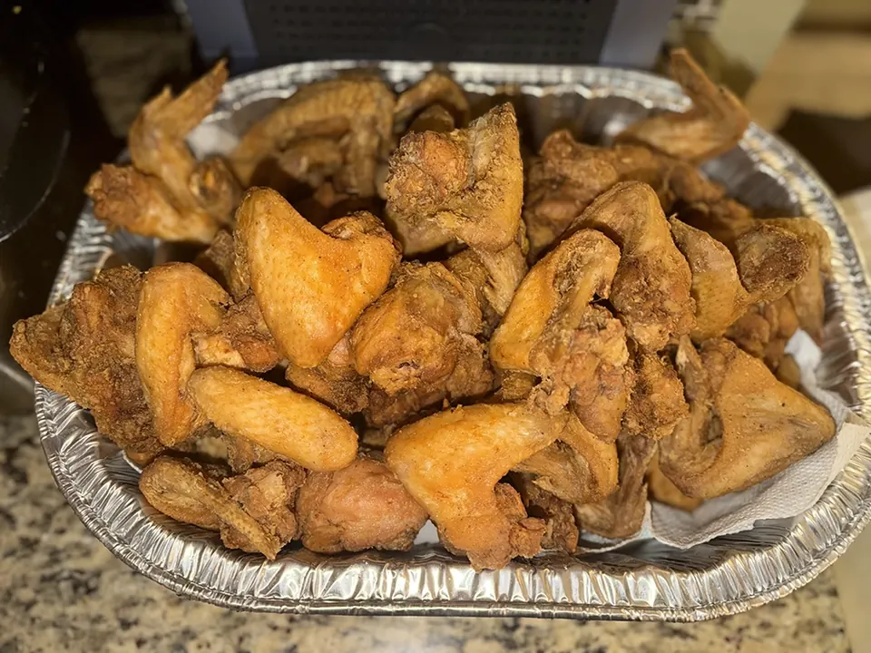 Golden chicken wings in a round foil serving pan